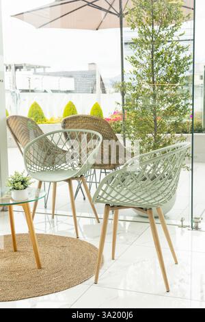 Eine stilvolle Terrasse in einem Gebäude mit eleganten Stühlen und modernem Sonnenschirm schafft einen eleganten Außenbereich zum Entspannen und Genießen. Stockfoto