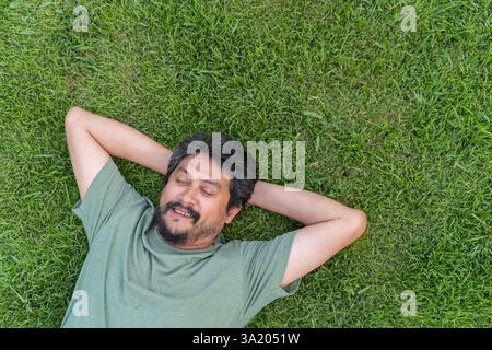 Hübscher junger Mann, der auf dem Boden liegt und sich mit geschlossenen Augen im Park entspannt. Junger Mann im Gras. Junger Mann, der in der Natur schläft. Stockfoto