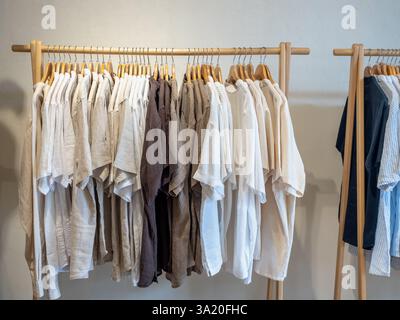 Kollektion aus weiß, Khaki, Erdfarbe, minimalem Stil von Relax Hemd in Kleiderbügeln, die an einer Kleiderstange aus Holz hängen, oder Kleiderständer auf weißem B Stockfoto