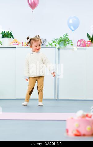 Niedliches 3-jähriges Mädchen mit Down-Syndrom feiert ihren Geburtstag in einem mit Ballons dekorierten Spielzimmer. Kindergeburtstag. Stockfoto