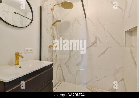 Ein modernes Bad mit eleganter Dusche, stilvollen goldenen Armaturen und minimalistischen Designelementen. Die Marmorfliesen verstärken das luxuriöse Ambiente des Raumes. Stockfoto