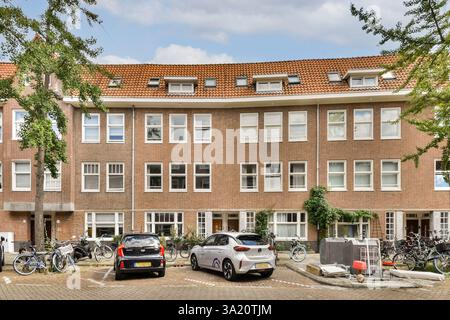 Ein modernes Wohngebäude mit großen Fenstern, umgeben von geparkten Fahrrädern und Autos. Die Architektur fügt sich nahtlos in das Grün im Freien ein. Stockfoto