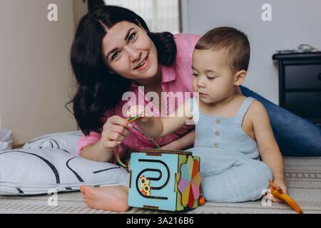 Mutter und Baby spielen zusammen mit Entwicklungsspielzeug, sitzen auf dem Boden, fördern das Lernen. Hochwertige Fotos Stockfoto