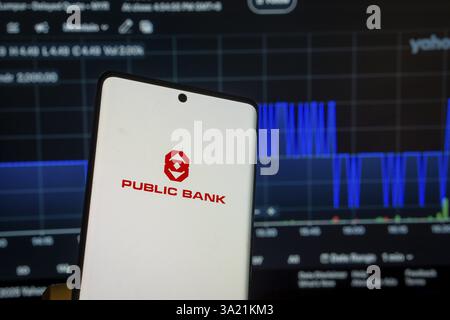 Dhaka, Bangladesch 08. März 2025: Bildschirm des Public Bank Logos auf einem Smartphone und der Finanzmarktplan im Hintergrund Stockfoto