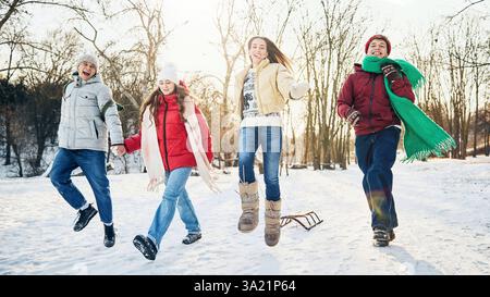 Eine Gruppe von Freunden springt fröhlich in den Schnee und teilt gemeinsam verspielte Wintermomente in einem öffentlichen, von Schnee bedeckten Park. Stockfoto