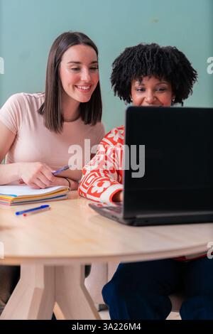 Zwei multiethnische junge Freundinnen, die zu Hause mit einem Laptop zusammen studieren Stockfoto