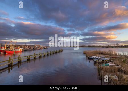 Sonnenuntergang über dem kleinen Dorf Zoutkamp in den Niederlanden mit Reflexionen des Himmels im Kanal und Fischereifahrzeugen im Hintergrund. Stockfoto