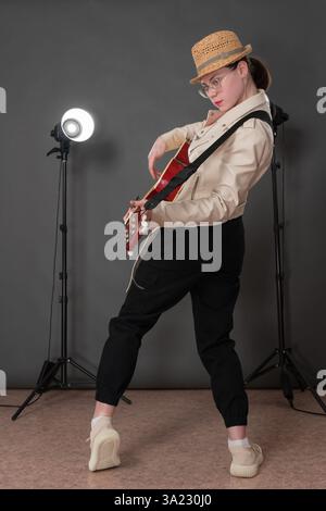 Dynamische Frauengitarristin spielt eine Akustikgitarre und blickt direkt in die Kamera. Die Seitenansicht der Frau ist der Hauptfokus der Aufnahme. Tragen von Musikern Stockfoto