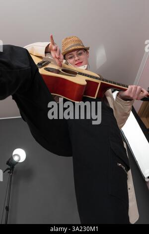 Eine Gitarristin, die spanische 6-saitige Akustikgitarre mit Blick in die Kamera spielt. Außergewöhnliches Niedrigwinkelbild, Weitwinkelperspektive für spielerische Musikszenen Stockfoto