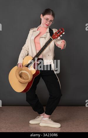 Weibliche Gitarristin mit klassischer Gitarre in Plie-Position wie Ballerina, die in voller Länge steht und in die Kamera blickt. Die Musikerin ist in Beige gekleidet Stockfoto