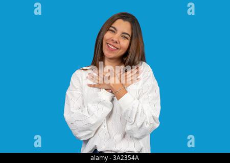 Studio-Porträt einer dankbaren jungen Frau, die ihre Hände auf der Brust hält, lächelt und dankbar und hoffnungsvoll ist Stockfoto
