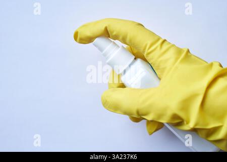 Hand in gelbem Handschuh, der die weiße Sprühflasche zur Reinigung oder Desinfektion vor hellem Hintergrund hält. Stockfoto