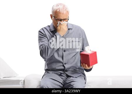 Mann im Pyjama, der sich mit Papiertüchern auf weißem Hintergrund die Nase bläst Stockfoto