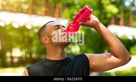 Durstiger schwarzer Mann, der nach seinem Wasser aus der Sportflasche trinkt Training im Park Stockfoto