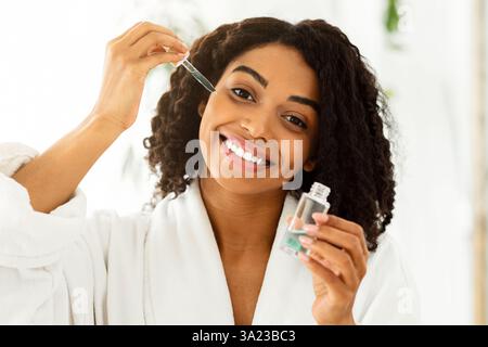 Hautpflegekonzept. Lächelnde Afrikanische Frau Holding Flasche Mit Feuchtigkeitsspendenden Serum Stockfoto