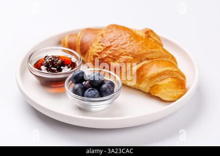 Knuspriges goldenes Croissant, serviert mit frischen Heidelbeeren und einer Beilage süßer Beerenmarmelade für ein köstliches Frühstück oder einen Snack Stockfoto