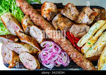 Auf einer lebendigen Platte gibt es eine Auswahl an gegrilltem Fleisch, darunter Würstchen und Spieße, begleitet von frischem Salat, Zwiebelscheiben und Fladenbrot, Stockfoto