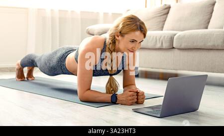 Sportliche Aktivitäten zu Hause allein. Frau sieht Fitness-Unterricht auf Laptop Stockfoto