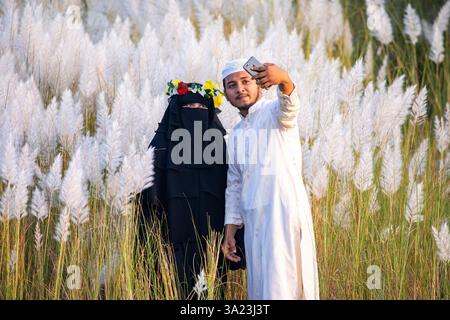 Ein muslimisches Paar, das in die Schönheit der blühenden Kans-Grasblumen eintaucht und das Wesen des Herbstes am Stadtrand von Dhaka, Bangla, feiert Stockfoto