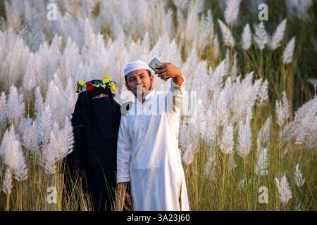 Ein muslimisches Paar, das in die Schönheit der blühenden Kans-Grasblumen eintaucht und das Wesen des Herbstes am Stadtrand von Dhaka, Bangla, feiert Stockfoto