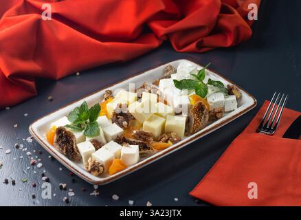 Plateau mit verschiedenen Käsesorten mit getrockneten Früchten und getrockneten Aprikosen, Feigen auf dunklem Hintergrund. Menü für einen Pub. Menü für ein georgianisches Restaurant. Stockfoto