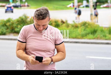 Mann, der auf einer Stadtstraße steht und das Handy benutzt Stockfoto
