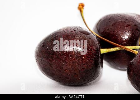Schwarze Kirschen auf weißem und hölzernem Hintergrund Stockfoto