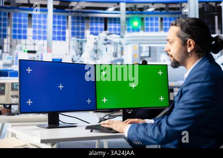 Ingenieur in der Photovoltaik-Fabrik überprüft Systemprotokolle auf isolierten Bildschirmen, um Fehler zu identifizieren. Photovoltaik-Anlagenarbeiter, der Fertigungsparameter auf PC-Monitoren anpasst Stockfoto