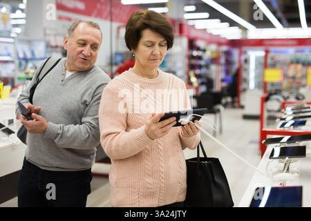 Seniorenpaar, das sich für Smartphone und Tablet im Tech-Store entscheidet Stockfoto