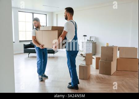 Eine große schwere Box. Zwei umziehende Servicemitarbeiter in einem Raum. Stockfoto
