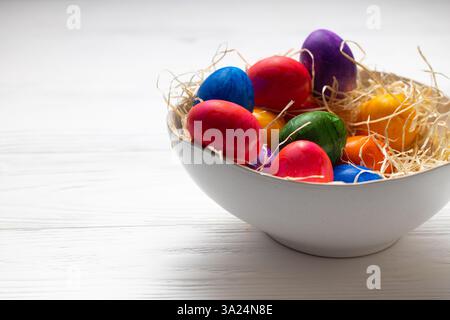 Bunte Ostereier auf einem weißen Teller auf einem weißen Holztisch Stockfoto