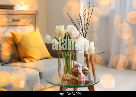Wunderschöne Tulpen mit Osterhase und Eiern auf Glastisch im Wohnzimmer Stockfoto