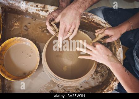 Menschen, Hände und Formen Töpferwaren im Atelier, arbeiten zusammen und schnitzen Ton für keramisches Kunsthandwerk. Draufsicht, Ausrüstung und Hilfe bei der Lektion bei Stockfoto