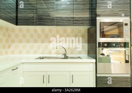Kleine, moderne Küche mit Mikrowelle, weißen Schränken und gemusterten Fliesen. Stockfoto