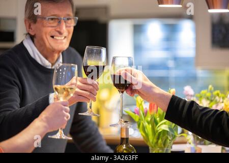 Ein lächelnder Mann trinkt Rotwein mit Freunden in der Küche. Stockfoto