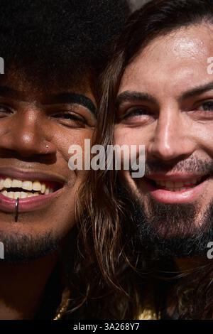 Zwei androgyne, nicht-binäre Menschen, die verliebt sind, lächeln fröhlich, während sie ihre einzigartigen Piercings und lebendigen Persönlichkeiten präsentieren Stockfoto