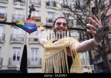 Glückliche nicht-binäre Person mit langen Haaren und Bart, die ein Selfie mit Smartphone macht, um den Stolz der Schwulen mit der Regenbogenfahne in chueca, madrid, zu feiern Stockfoto