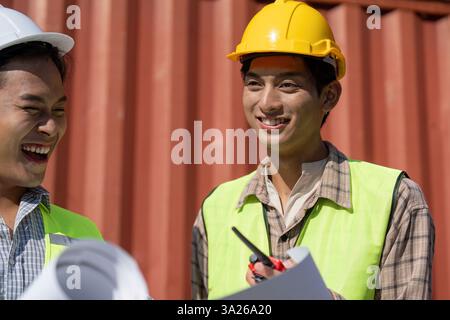 Engagierte Ingenieure. Ingenieure lachen und überprüfen Pläne an einem Logistikstandort. Stockfoto