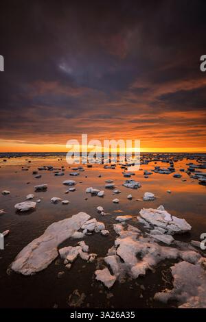 Das Wattenmeer ist im Winter mit Eisschollen bedeckt. Ein wunderschöner Sonnenuntergang färbt den Himmel mit atemberaubenden Farben Stockfoto