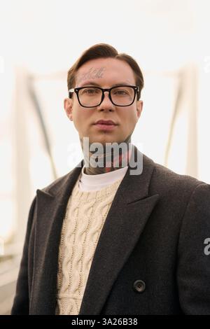 Der gutaussehende Mann strahlt Selbstvertrauen aus, während er ein trendiges Outfit trägt und seine Tattoos zeigt. Stockfoto