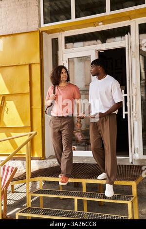 Ein liebevolles Paar geht Hand in Hand und teilt ein Lächeln vor einem einladenden Café mit sonnigem Flair. Stockfoto