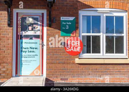 Vordertür und Fensterblick eines neu erbauten Hauses zum Verkauf. Persimmon Hausbauer Schilder vor dem neuen Haus mit einem großen roten Schild zum Verkauf und plo Stockfoto