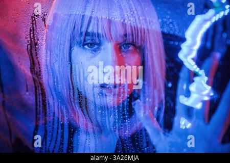 Vorderansicht. Stilvolle Frau mit weißem Haar steckt hinter nasser transparenter Plastikfolie. Stockfoto