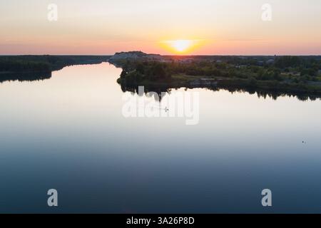 Sommersonnenuntergang in Rummu: Zwei Personen auf Paddleboards genießen den feurigen Himmel über dem ruhigen Wasser dieses erstaunlichen Steinbruchs. Stockfoto