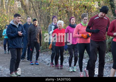 Eine vielfältige Gruppe von Erwachsenen in sportlicher Kleidung nimmt an einer Gruppenübung im Freien in einer Waldumgebung Teil. Sale Water Park, Manchester, Großbritannien Stockfoto