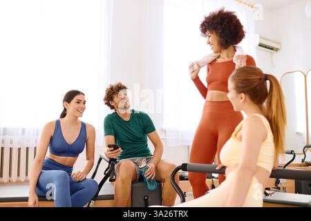 In einem sonnigen Pilates-Studio teilen Freunde nach einem energischen Kurs ein Lächeln und ermutigen sie. Stockfoto