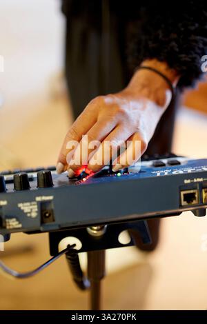Eine Hand stellt die Bedienelemente eines blauen Audiomischers in einem Aufnahmestudio ein, wobei die Regler und Leuchtanzeigen im Fokus stehen. Stockfoto