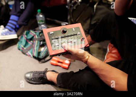 Hand hält einen roten Audiomischer in einem Aufnahmestudio, mit Schuhen, einem Rucksack und einer Flasche im Hintergrund. Stockfoto