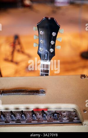 Elektrischer Gitarrenhals mit Stimmknöpfen über einem Vintage-Verstärker in einem Musikstudio. Stockfoto