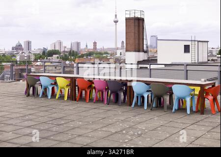Farbenfrohe Stühle, die um einen Tisch auf einem Dach angeordnet sind, mit einer Skyline der Stadt im Hintergrund. Berlin, Deutschland Stockfoto